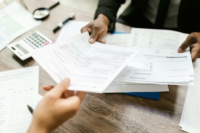People exchanging documents at a desk, symbolizing industries built on fooling people, with a calculator in the background.