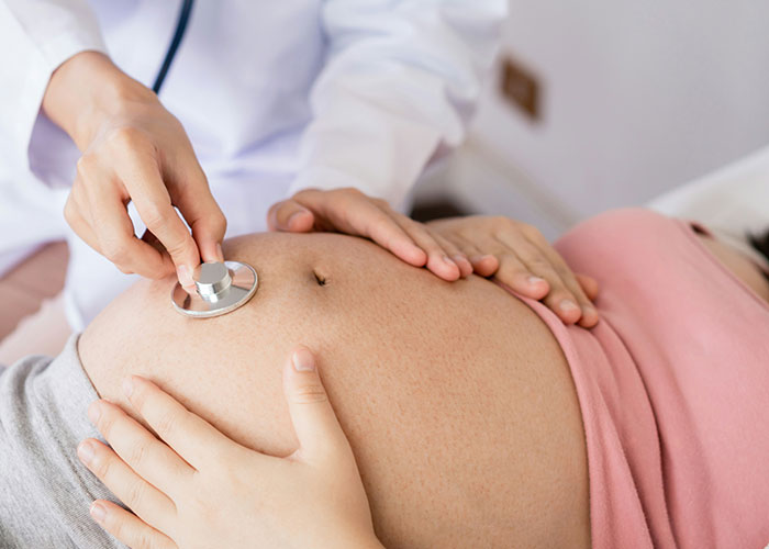 Doctor examining pregnant belly with stethoscope, illustrating hospital workers' experiences.