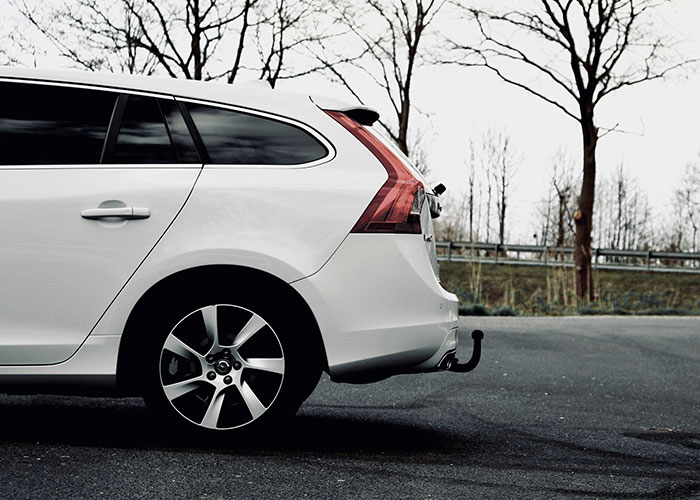White car parked on a road with leafless trees in the background.