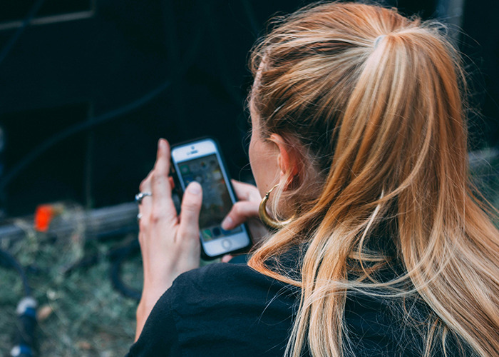 A woman with blonde hair using a smartphone, possibly reading about insurance horror stories.