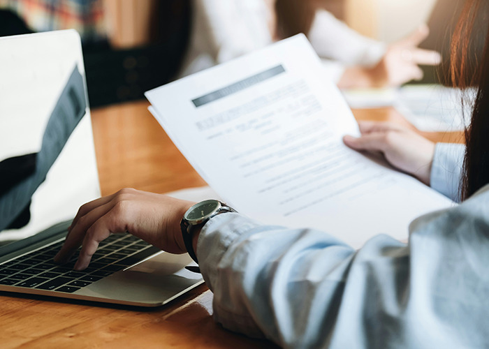 Person reviewing insurance documents, typing on a laptop; highlighting the real-life challenges of insurance claims.