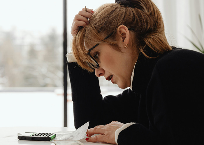 Woman stressed over insurance paperwork at a table, holding her head, with a calculator nearby.