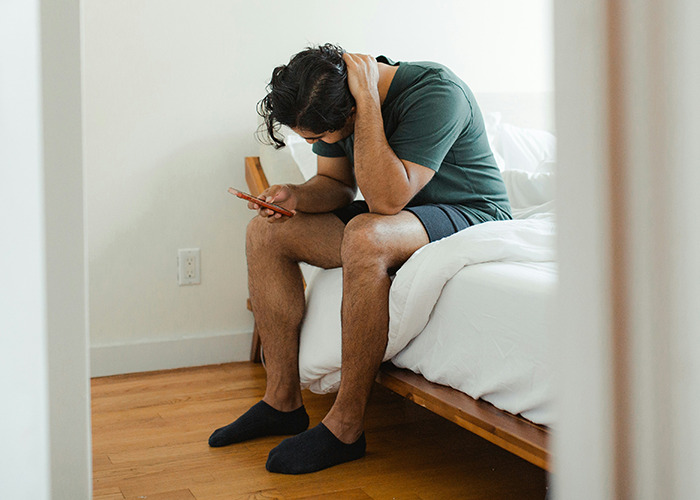 Man sitting on bed, looking stressed at phone, related to insurance horror stories.
