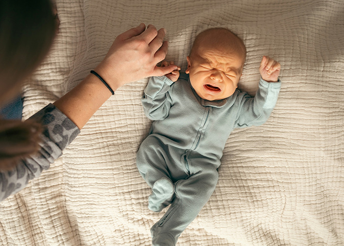 Crying baby on a bed, held by an adult, illustrating a scene related to insurance horror stories.