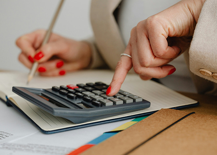 Hands of a person calculating insurance costs on a calculator with red nails.
