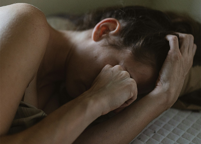 A person lying in bed, appearing distressed, representing real-life insurance horror stories.