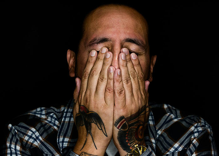 A distressed man with tattoos covers his face, illustrating real-life insurance horror stories.