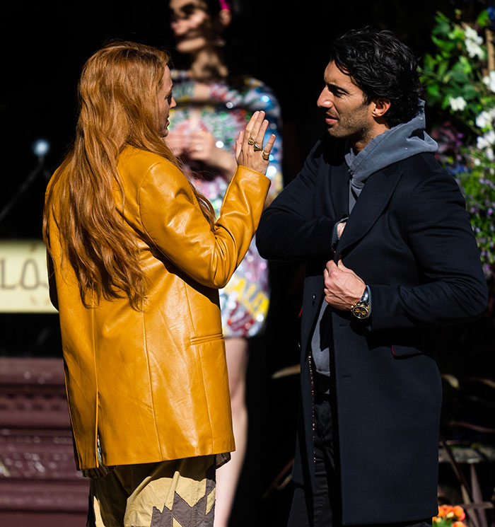 Man and woman talking outdoors, both in stylish jackets, for a scene involving discussions around Justin Baldoni. Man and woman talking outdoors, both in stylish jackets, for a scene involving discussions around Justin Baldoni.