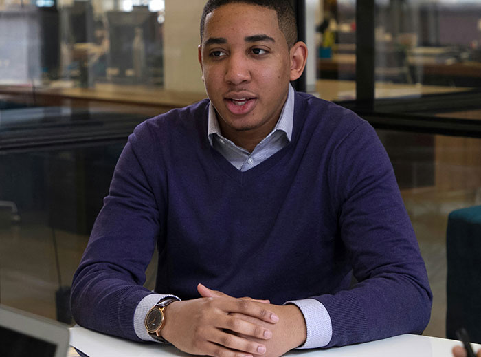 Candidate at job interview, seated, wearing a purple sweater, with a serious expression related to salary expectations.