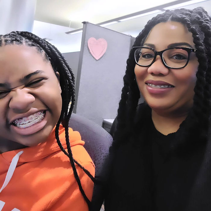 Kelaia Turner in an orange hoodie, mom Ty Turner in glasses, in an office setting with a heart decoration on the wall. Kelaia Turner in an orange hoodie, mom Ty Turner in glasses, in an office setting with a heart decoration on the wall.