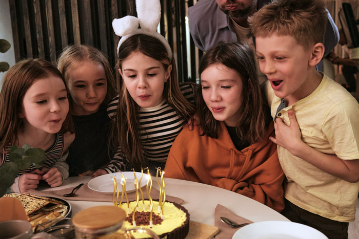 Kids blowing out birthday cake candles, surrounded by friends, creating a festive party scene.