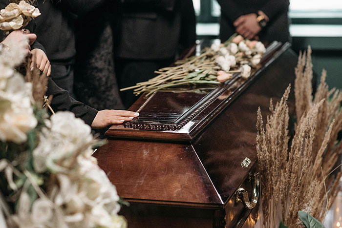Funeral scene with a hand on a wooden casket and flowers, related to life insurance repayment discussion. Funeral scene with a hand on a wooden casket and flowers, related to life insurance repayment discussion.