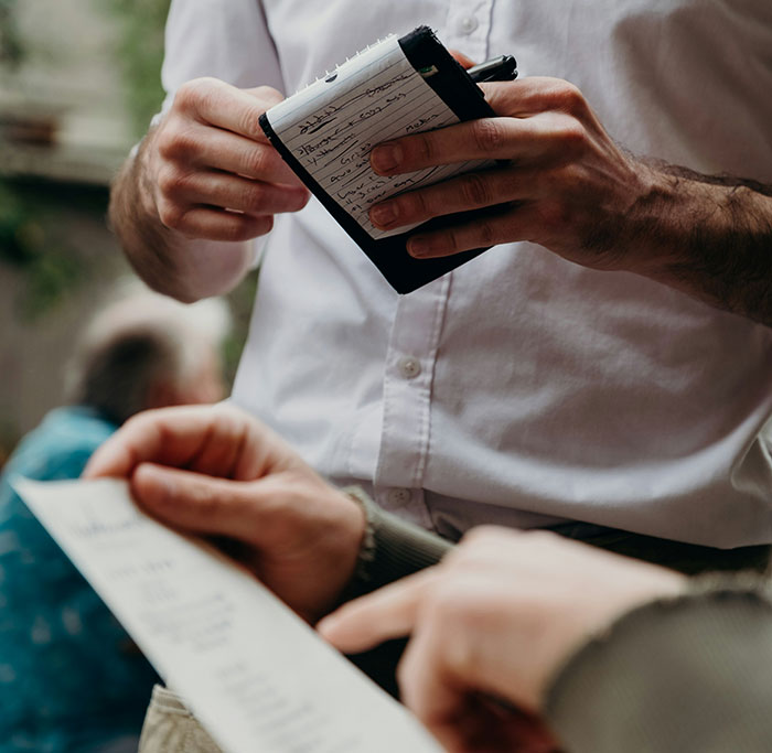 Person holding notebook, taking notes from someone pointing at a menu, depicting unattractive behaviors.