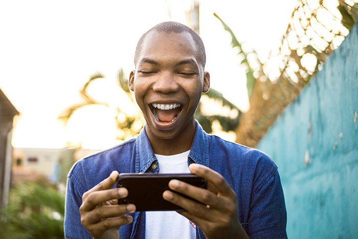 Man smiling while looking at a smartphone outside, wearing a denim jacket.