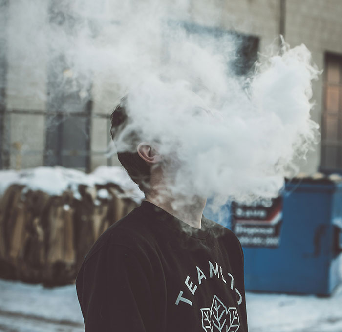 Person exhaling a thick cloud of smoke outdoors, highlighting unattractive behavior.