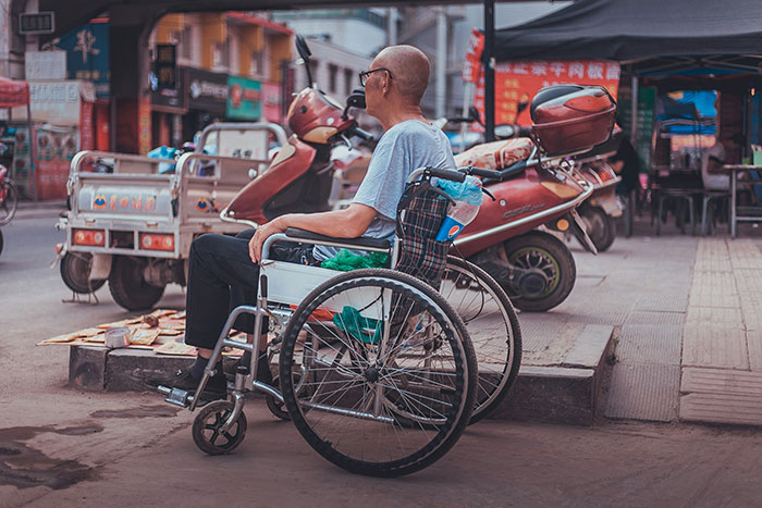 Man in a wheelchair on a city street next to parked scooters.