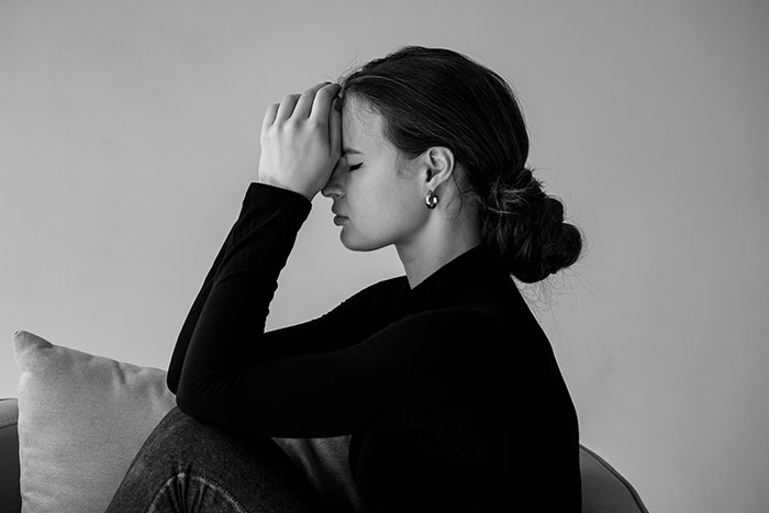 Woman appearing frustrated, sitting with head in hand, expressing unattractive behavior in monochrome setting.