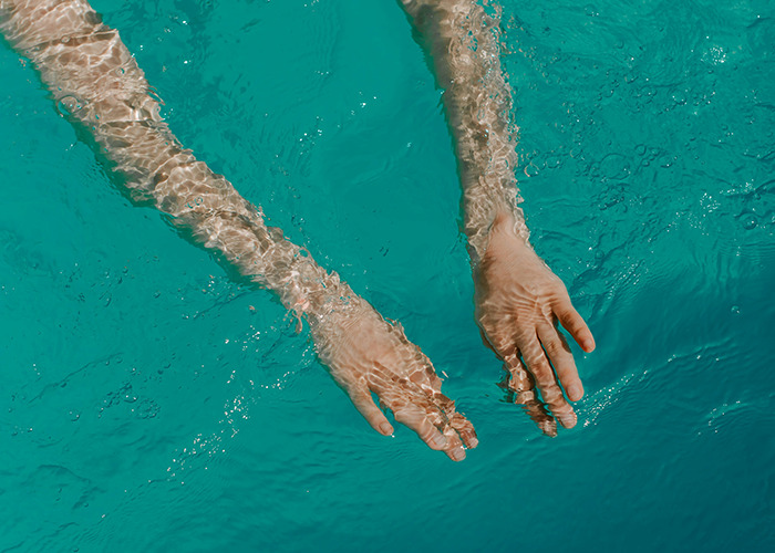 Hands submerged in clear water, illustrating health benefits of swimming as a simple exercise hack.
