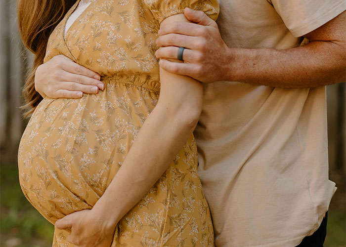Pregnant woman in yellow dress embraced by partner, symbolizing a life-changing event.