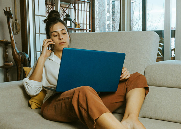 Woman on phone working on a laptop while sitting on a couch, symbolizing life-changing events and multitasking skills.