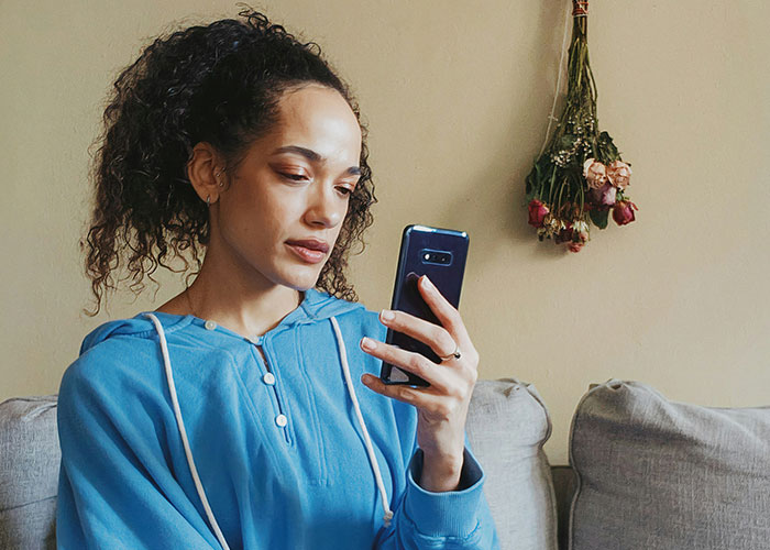 Woman in a blue hoodie sitting on a couch, looking at her phone thoughtfully; life-changing moments concept.