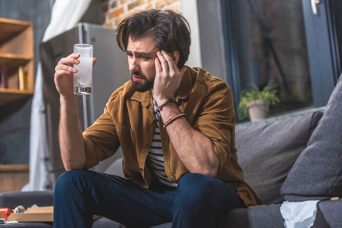 Man on couch holding a glass, looking distressed, symbolizing getting fired unexpectedly.
