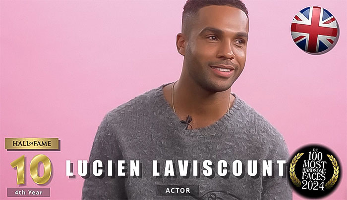 "Man in gray sweater, ranked among the most handsome men of 2024 by The Independent Critics, smiling on pink background.