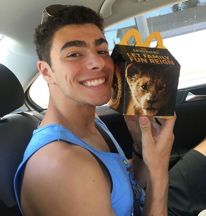 Luigi Mangione in a car, holding a McDonalds fast-food box featuring a lion cub image.