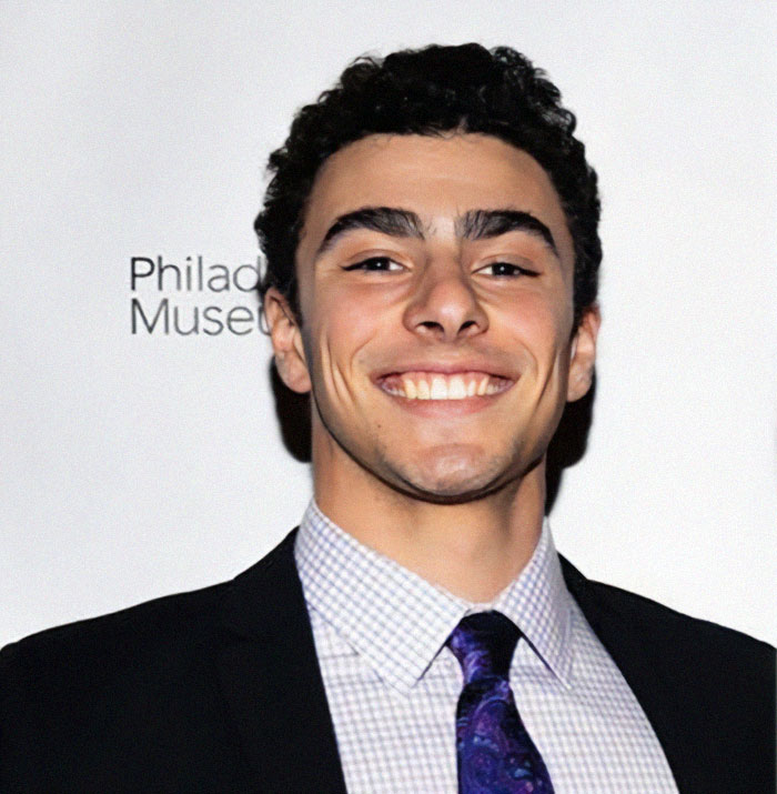 Luigi Mangione in formal attire at an event, with a backdrop featuring museum branding.
