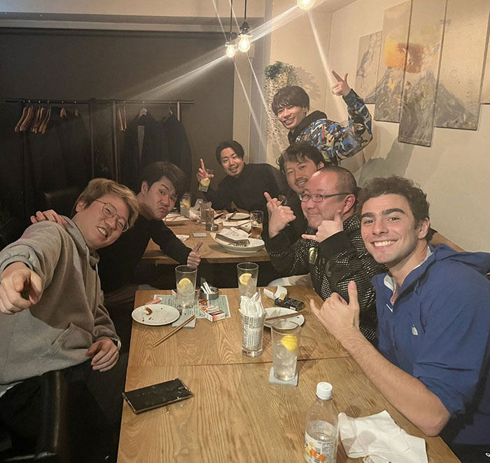 A group of friends smiling and posing around a dining table in a cozy restaurant setting.