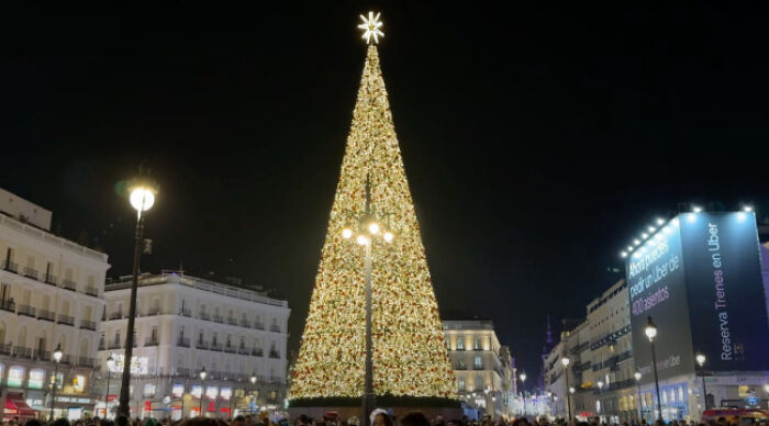 Illuminated Christmas tree in a city square at night, showcasing festive decorations and bright lights.