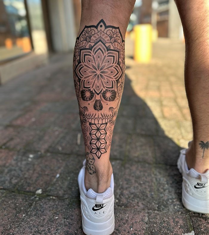 Mandala tattoo with a skull design on a leg, showcasing intricate patterns and artistic placement.