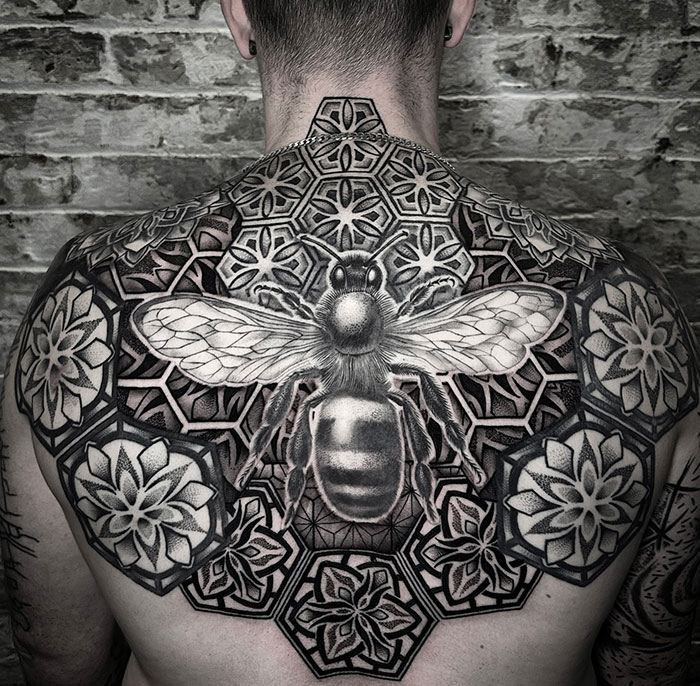 Back with a mandala tattoo featuring a bee, showcasing intricate geometric patterns.