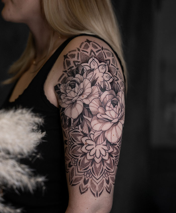Intricate mandala tattoo design on a woman's upper arm, showcasing floral patterns and detailed line work.
