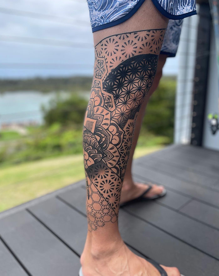 Leg with intricate mandala tattoo design, showing geometric patterns and shading, outdoors on a deck.