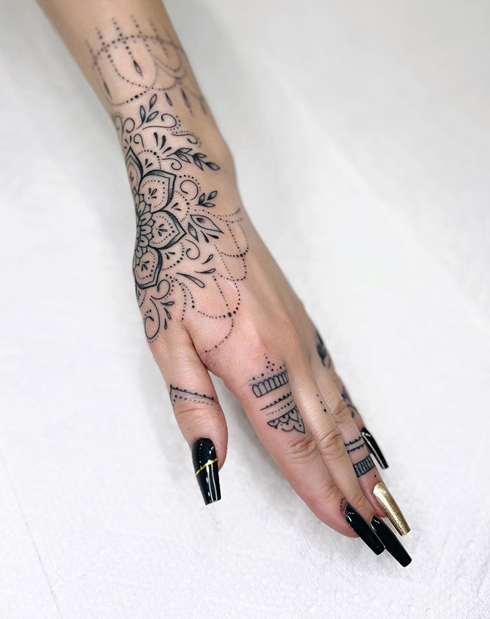 Hand with intricate mandala tattoo design, featuring floral patterns and dots, placed elegantly on the back of the hand.