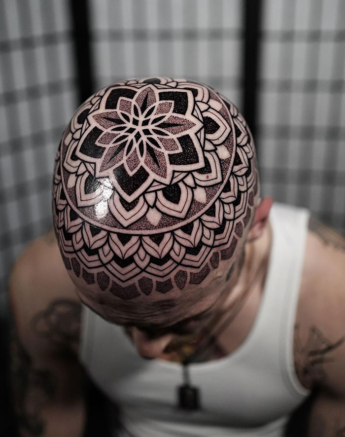 Intricate mandala tattoo design covering the entire scalp of a man wearing a white tank top.