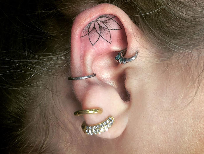 Ear with multiple piercings and a delicate mandala tattoo inside, showcasing unique placement and design ideas.