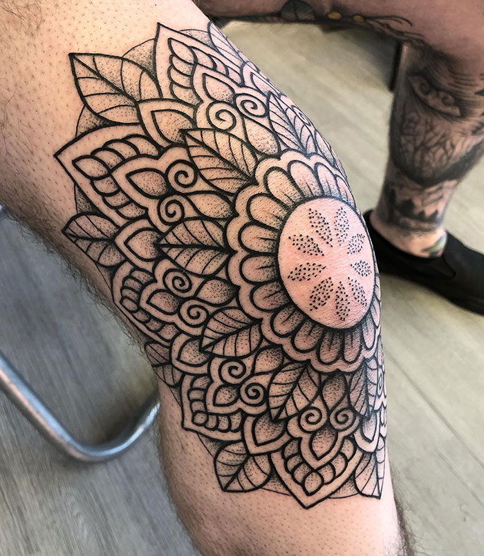Intricate mandala tattoo design covering a person's knee, showcasing detailed patterns and symmetry.