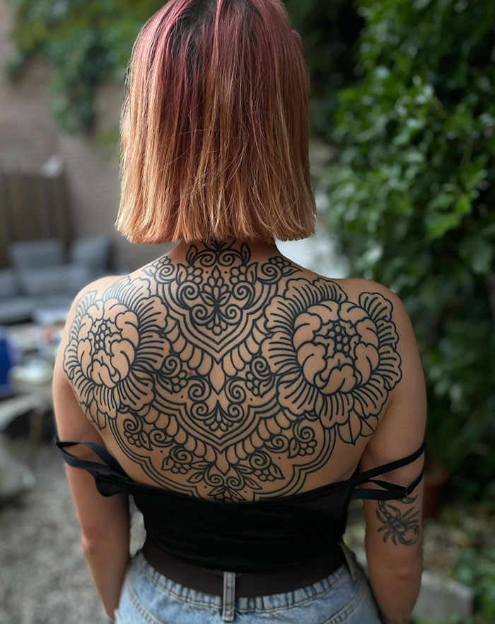 Woman's back with an intricate mandala tattoo, showcasing elaborate design and placement.