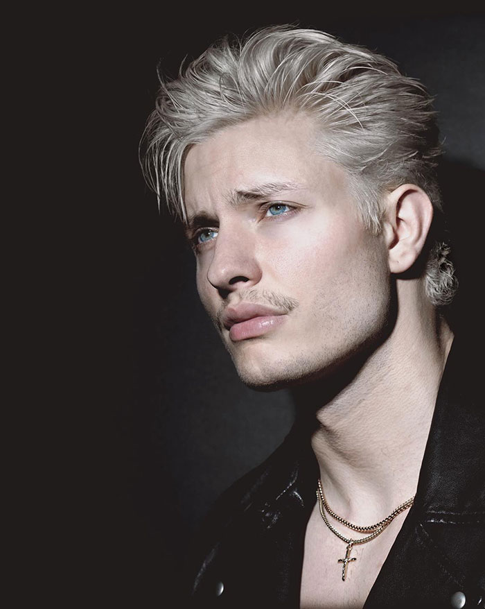 Matt Rife with a drastically different look, wearing a leather jacket and gold necklace, in a dimly lit setting. New comedy special poster