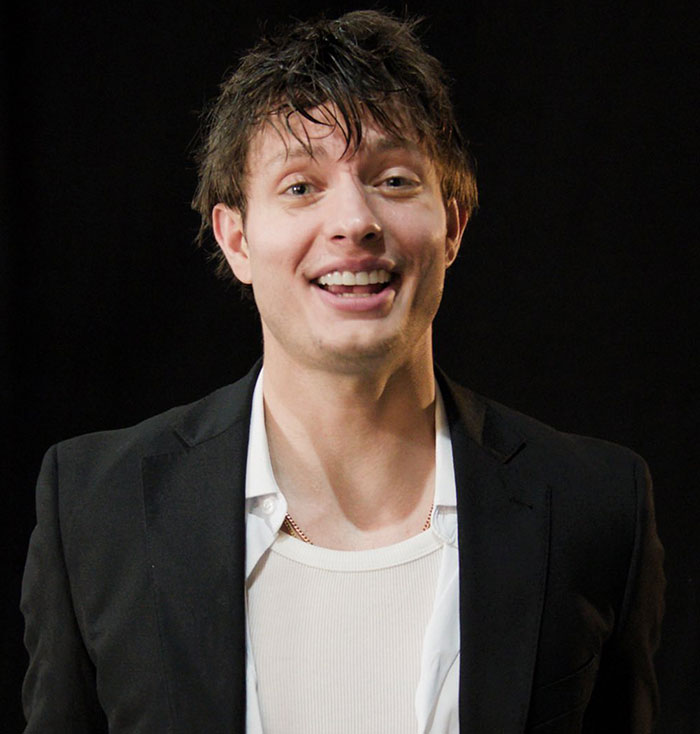 Comedian Matt Rife smiling in a black jacket, before dyeing his hair blonde