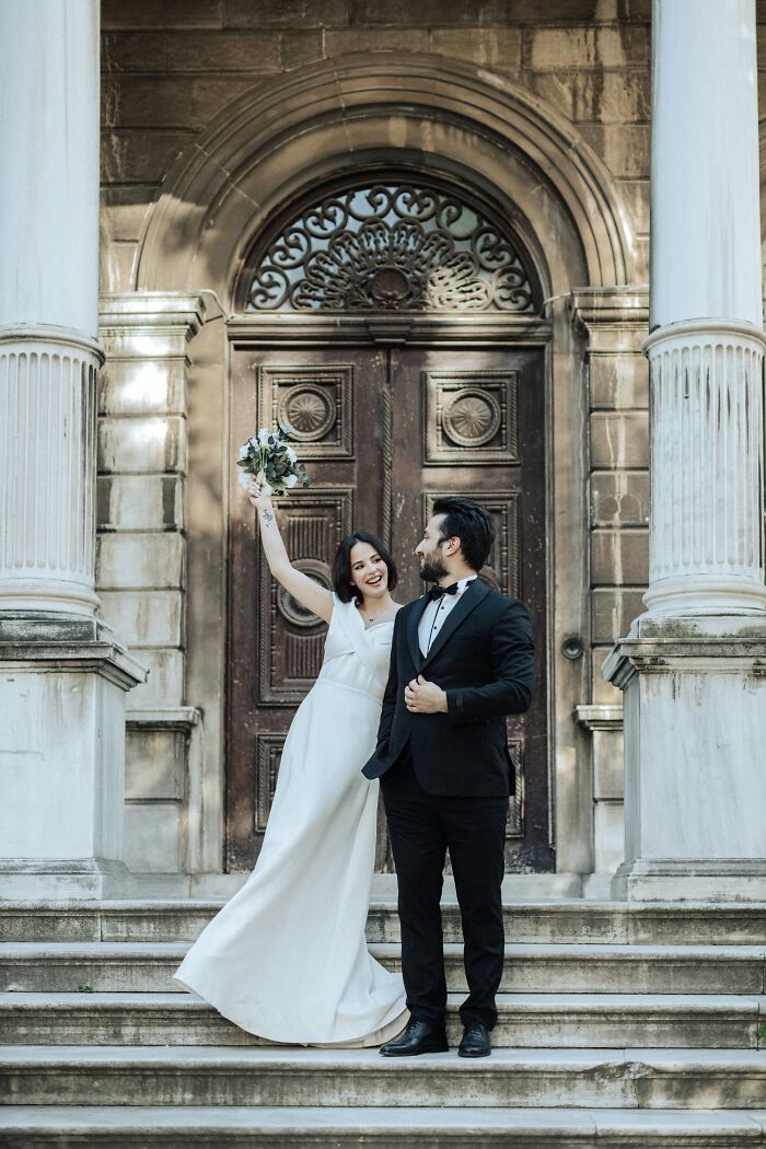 Couple in wedding attire smiling on steps with ornate wooden door, capturing a life-altering moment.