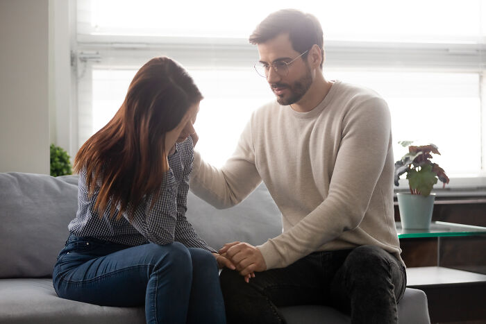 A man comforting a stressed pregnant woman on a couch, highlighting Christmas-related stress.
