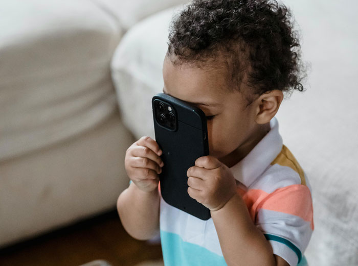 Toddler playing with a smartphone, capturing the curiosity and potential risk as the child holds it close to their face. Toddler playing with a smartphone, capturing the curiosity and potential risk as the child holds it close to their face.