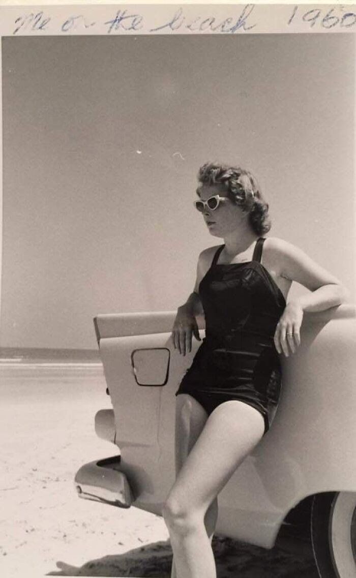 60s fashion look featuring a woman in a vintage swimsuit and sunglasses leaning on a classic car at the beach.