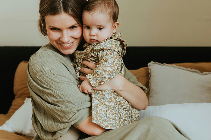 New mom holding baby, both in patterned outfits, on a cozy bed. New mom holding baby, both in patterned outfits, on a cozy bed.