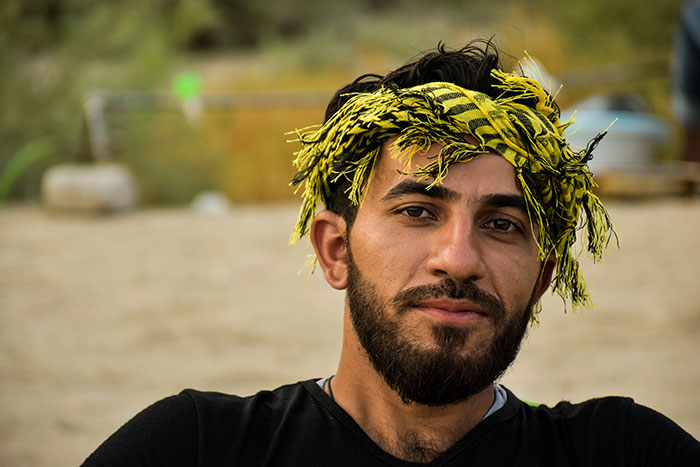 Portrait of a man with a beard wearing a yellow and black headscarf, reflecting a calm expression in a natural setting.