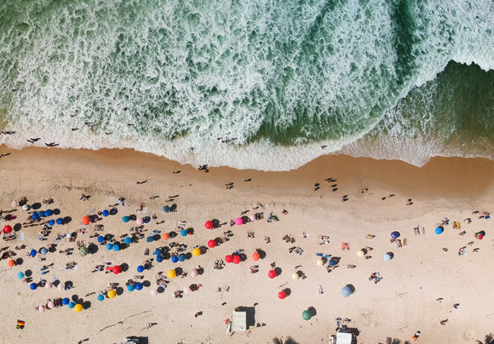 Aerial view of a crowded beach with colorful umbrellas and waves, highlighting beach activities.