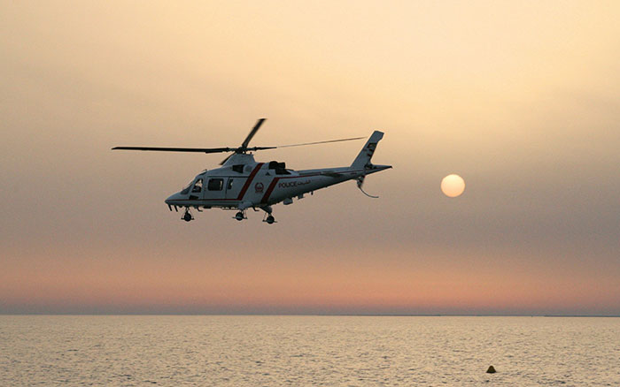Police helicopter flying over the beach during sunset.